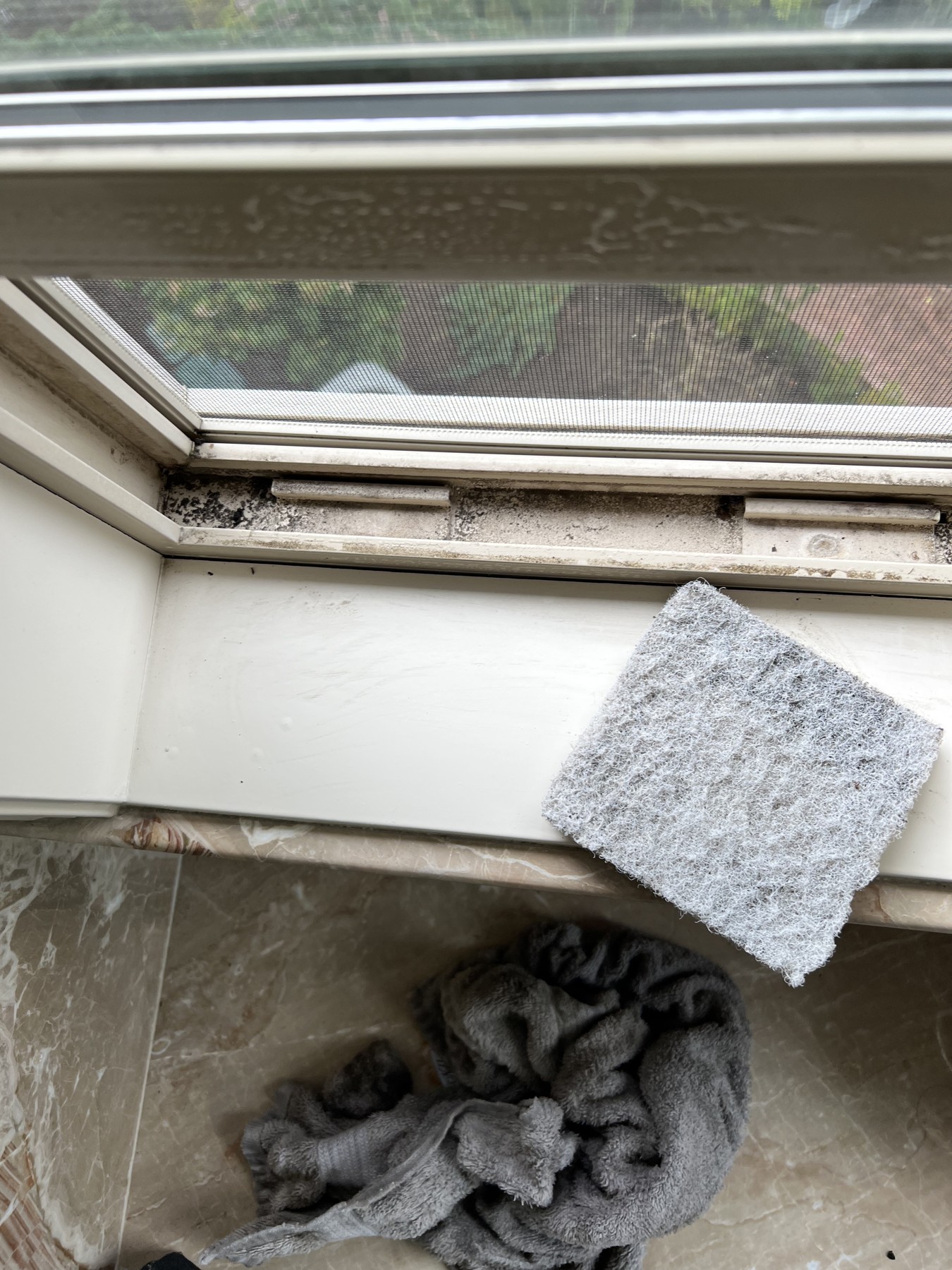 Dirty window track before cleaning, with a scrub pad beside the window